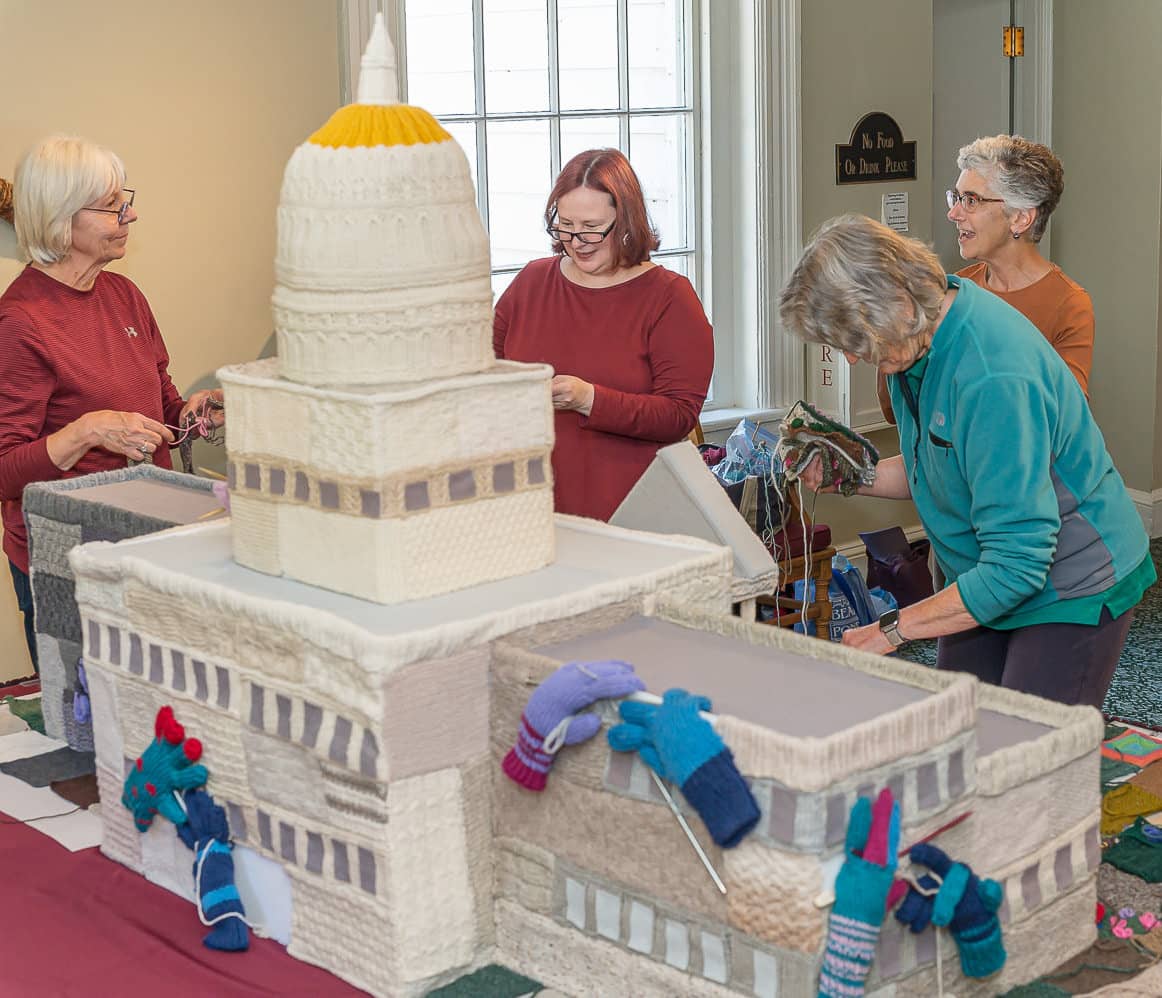 Four women working on the knitted sculpture of the Vermont State House.